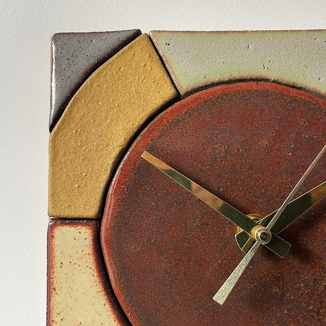Close-up of a modern geometric ceramic wall clock with a rusted reddish-brown circular face and angular ceramic segments in beige, gray, and cream around the edge.