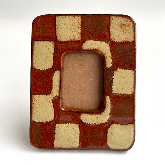 A square ceramic picture frame with a glossy checkered pattern in terracotta red and cream, featuring a central rounded rectangular cutout.