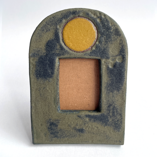A small decorative ceramic picture frame with an arched top, a round gold-toned moon at the top, and a rectangular opening below showing a warm tan interior, photographed on a plain white background.