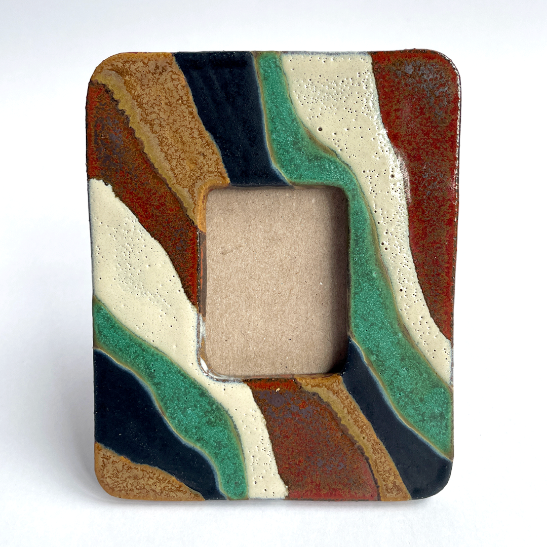A square ceramic picture frame with an abstract wavy pattern in terracotta, sage green, cream, brown, and black, featuring a rectangular cutout in the center.
