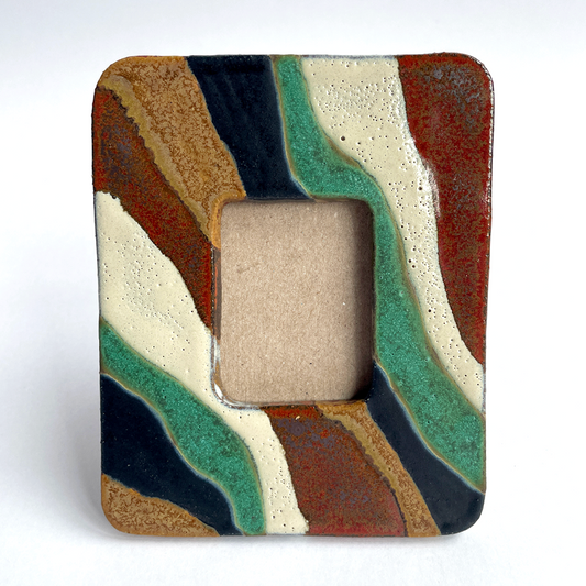 A square ceramic picture frame with an abstract wavy pattern in terracotta, sage green, cream, brown, and black, featuring a rectangular cutout in the center.