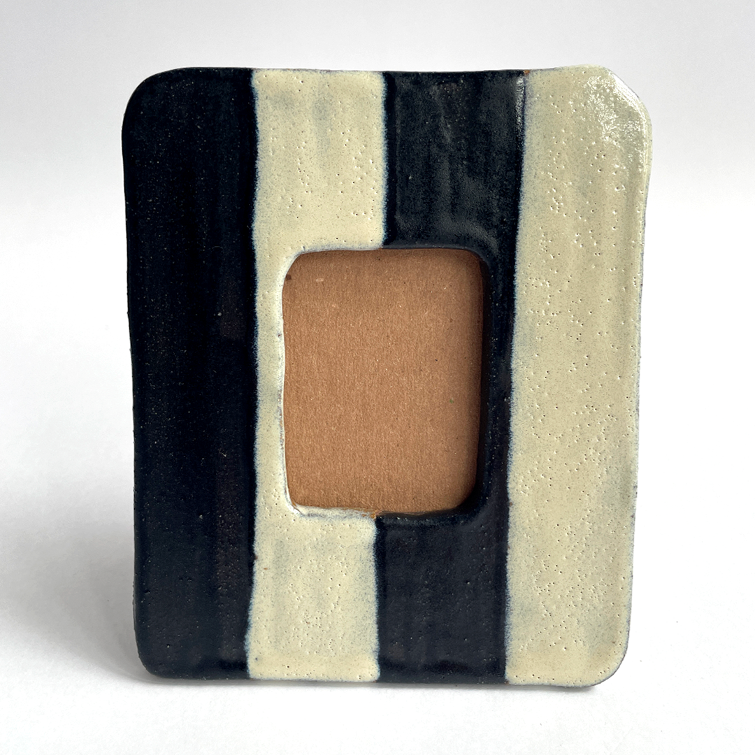 A square ceramic picture frame with a textured, hand-painted finish. The frame features four vertical stripes in glossy black and matte cream, with a central rectangular cutout showing a tan backing.