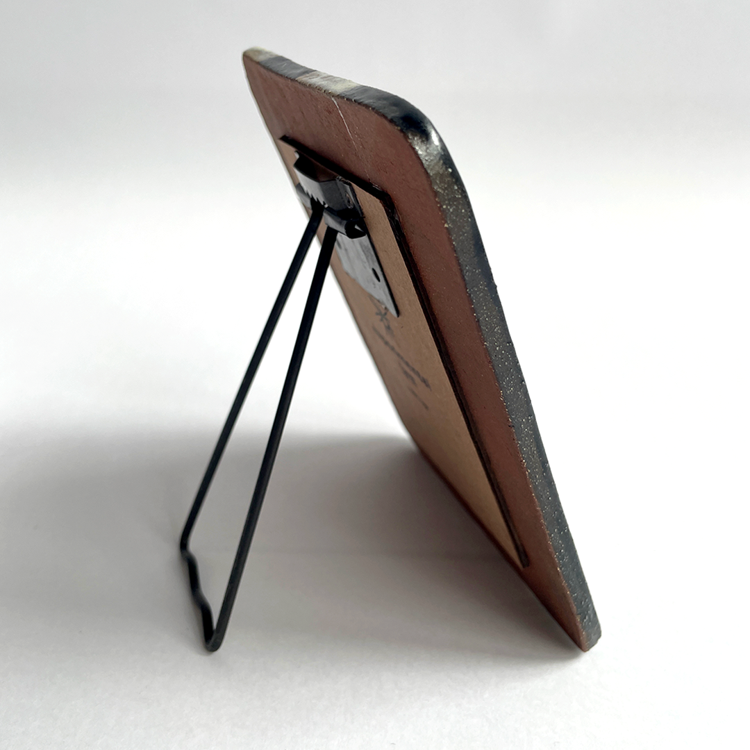 A small rectangular picture frame with a brown ceramic front, dark gray textured edges, and a black metal wire stand, shown on a white background.