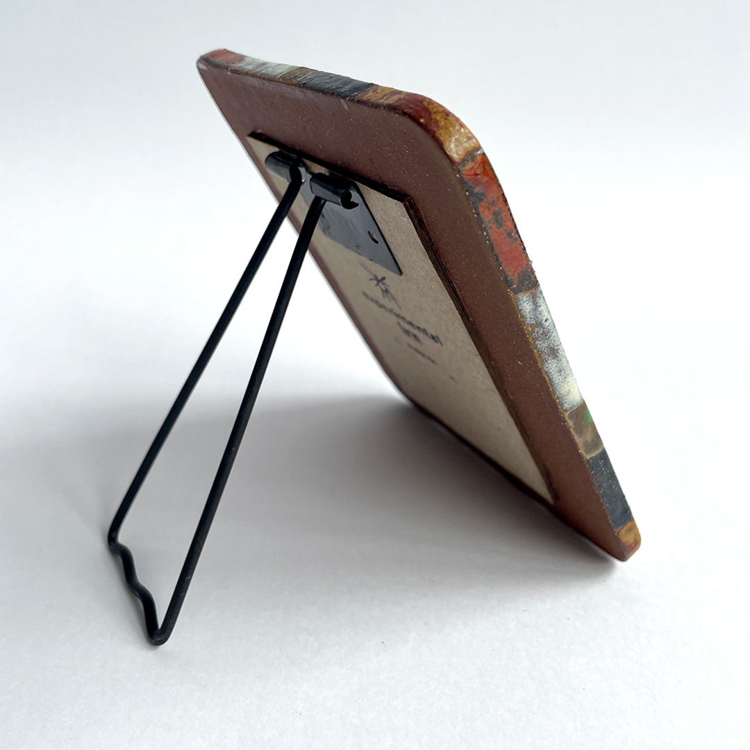 A small rectangular picture frame with a brown ceramic border and a black metal kickstand, shown from an angle on a white background.