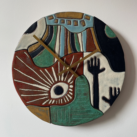 A round, hand-painted and hand-carved abstract ceramic wall clock with sculptural relief details and gold-tone hands, mounted on a plain white wall.